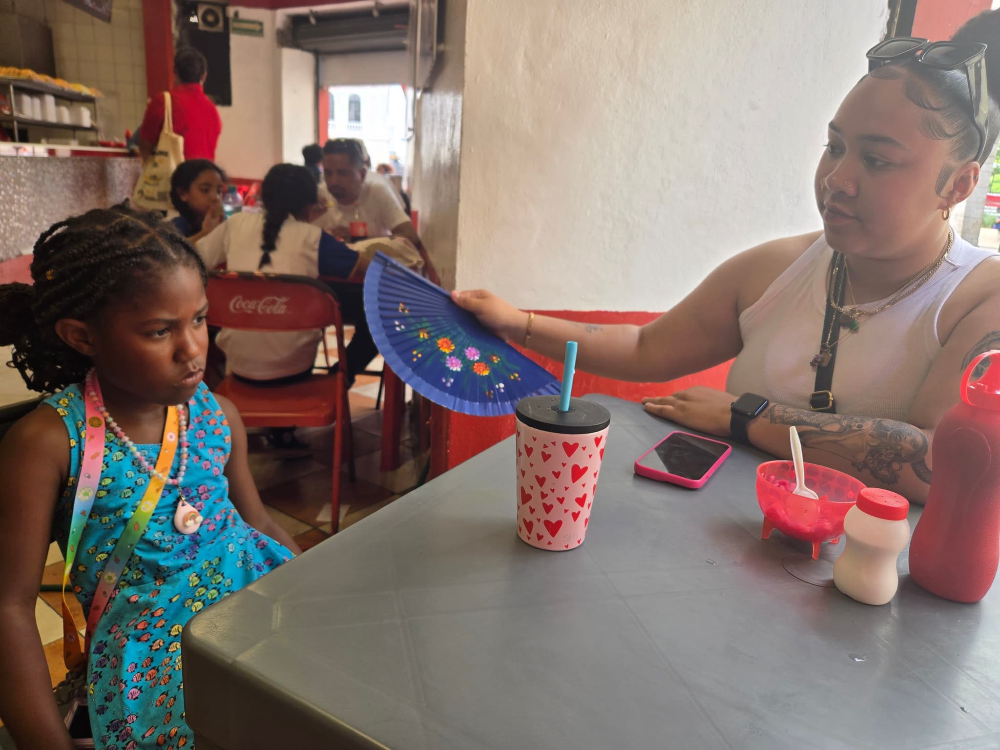 Maya fanning an angry Izzy in a restaurant"